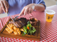 Man eating steak, chips and salad with beverage in background
